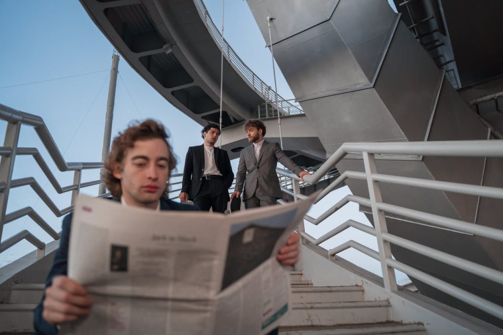 Three business professionals interact on outdoor stairs. One reads a newspaper while others walk and talk.